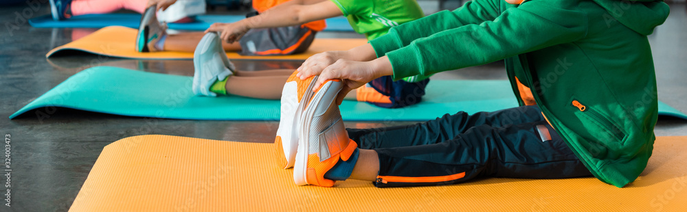 Cropped view of children stretching on fitness mats in sports center, panoramic shot