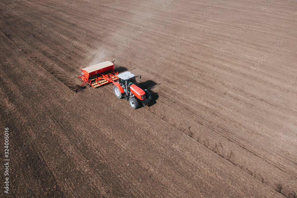 Aerial of red tractor plowing a field in countryside.
