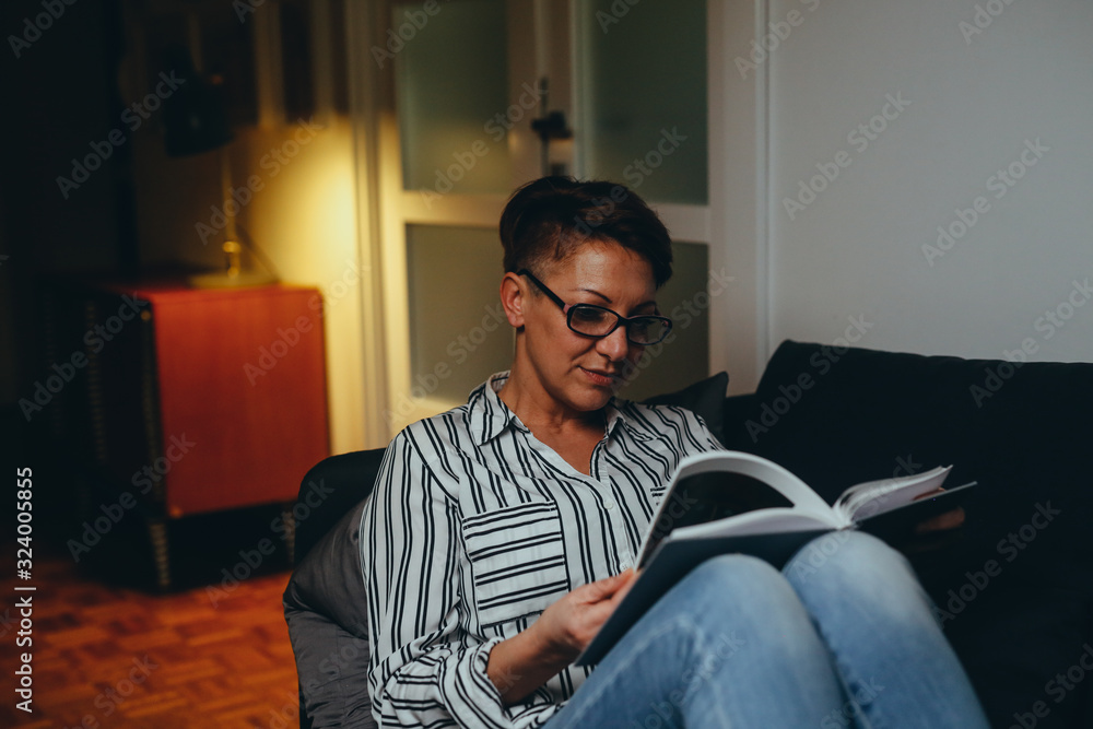 woman relaxed on sofa reading book, evening scene