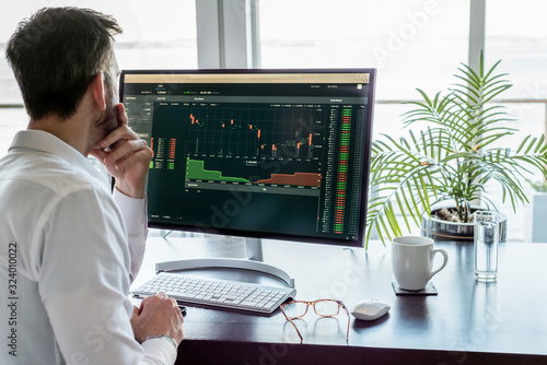 Man researching exchange market data on modern computer screen, desk with keyboard, mouse, eyeglasses and coffee. 