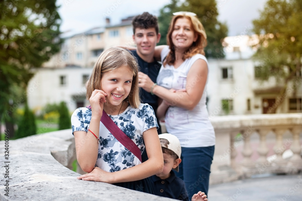 A woman with her children vacation in the summer. Focus on daughter posing for photographer, behind her mom and brother are also trying to get in the frame