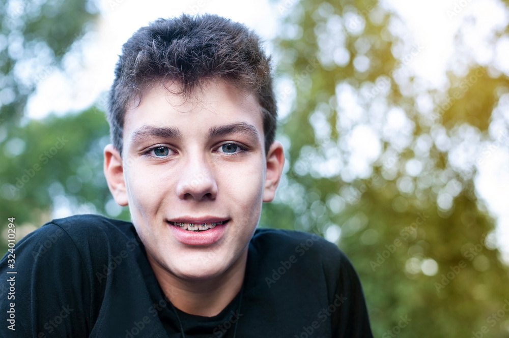 Portrait of a teenager boy on a background of trees and sky in the summer. The guy is resting in nature in the open air, he has braces on his teeth Portrait of a teenager boy on a background of trees and sky in the summer. The guy is resting in nature in the open air, he has braces on his teeth