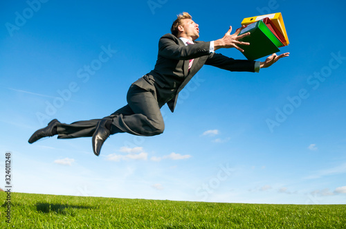 Careless office worker tripping dramatically with his file folders flying outdoors in a green grass field