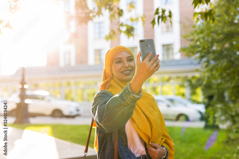 Muslim girl in hijab makes a selfie on the phone standing on the street of the city