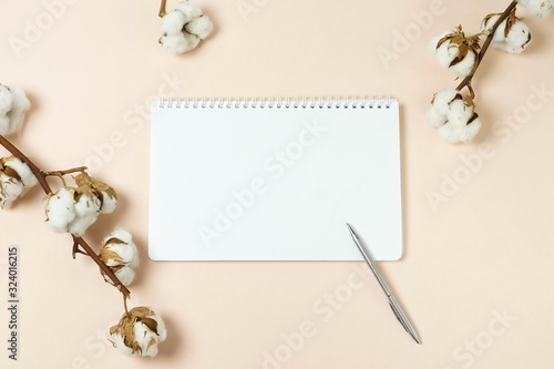 notebook mock up, pen , cotton flowers on beige background top view. copy space. pastel colors background