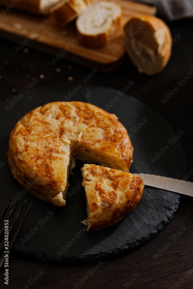 Spanish potato omelette on a black rounded chalkboard. Dark food still life image. Spanish potato omelette on a black rounded chalkboard. Dark food still life image.