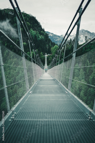 Young female crossing suspension rope bridge in alpine environment