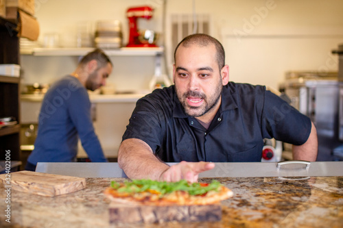 A chef leans over a kitchen counter describing a prepared dish of food photo