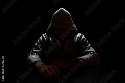 A man in a hood sits in the dark with arms extended forward. Crime and Internet Security photo