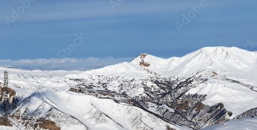 Panorama of snowy winter mountains and cloudy blue sky photo