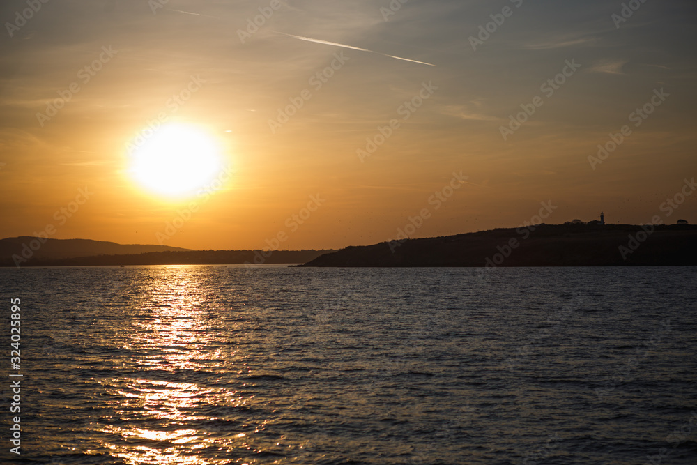 Sunset on the sea, seagulls fly over the waves and the outlines of the stone island. The orange light of the setting sun illuminates the gulls above the sea and the dark water of the Black sea