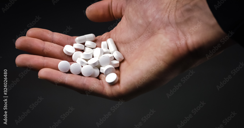 Holding medical pills and tablets and dropping them on black background Holding medical pills and tablets and dropping them on black background