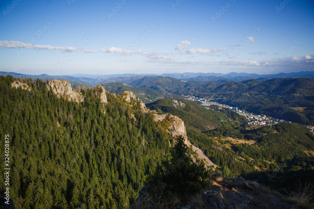 Panoramic top view of the green mountain valley from the top of the cliff in autumn in the Balkans. Mountain village in the Rhodope mountains in Bulgaria