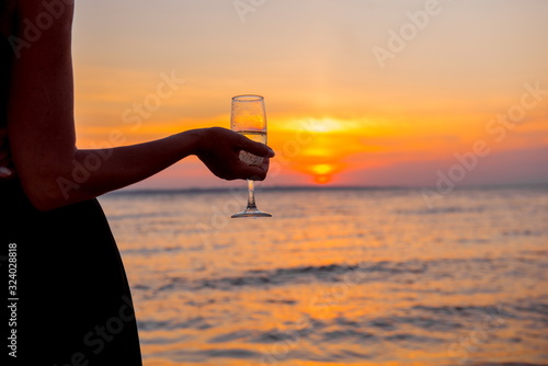 girl on the beach. Elegant girl is drinking champagne. hand with glass. woman at sunset. woman on the beach. Girl with glass on background setting sun. romantic date in the evening.