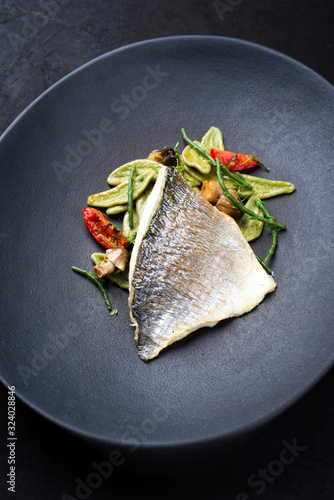 Gourmet fried Italian gilthead fish filet with spinach pasta, glasswort and tomatoes as closeup on a modern design plate
