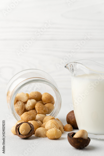 Dairy products without lactose. Scattered macadamia nuts on a white surface and macadamia milk in a glass cup. Vertical orientation with copy space. Dairy-free milk.
