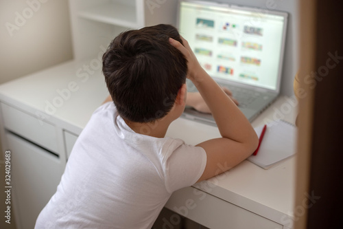 The boy sits with his back behind a laptop, looks on the Internet