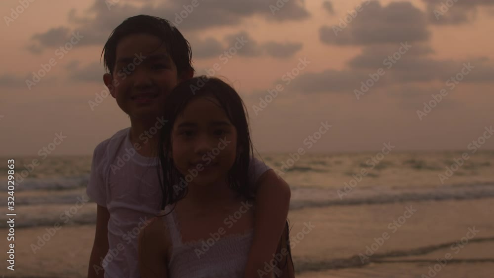 Asian young happy family enjoy vacation on beach in evening. Brother and sister smile and looking to camera relax together near sea silhouette sunset. Lifestyle travel holiday summer. 4k Slow motion. Asian young happy family enjoy vacation on beach in evening. Brother and sister smile and looking to camera relax together near sea silhouette sunset. Lifestyle travel holiday summer. 4k Slow motion.
