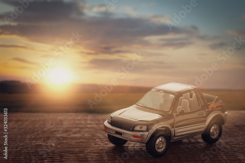 Toy car on a background of grass and sunset sky: the concept of road travel and car insurance