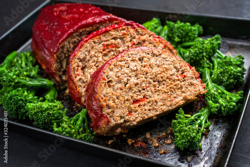 Traditional American meatloaf from ground beef with ketchup and broccoli as closeup on a rustic metal tray