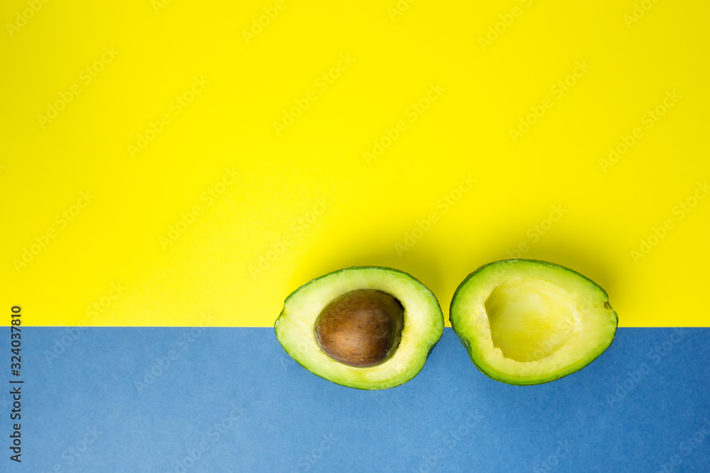 Green fresh avocado on isolated yellow and blue background. Vitamin, vegan food concept