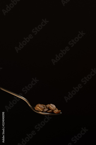 Black coffee beans in metal spoon on black background