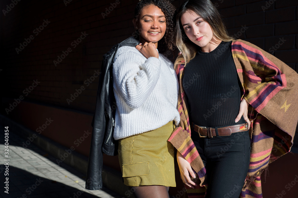 Obraz premium Portrait of two beautiful fashionable Hispanic girls, happy smiling posing for the camera. Autumn street art photo. Y, Z
