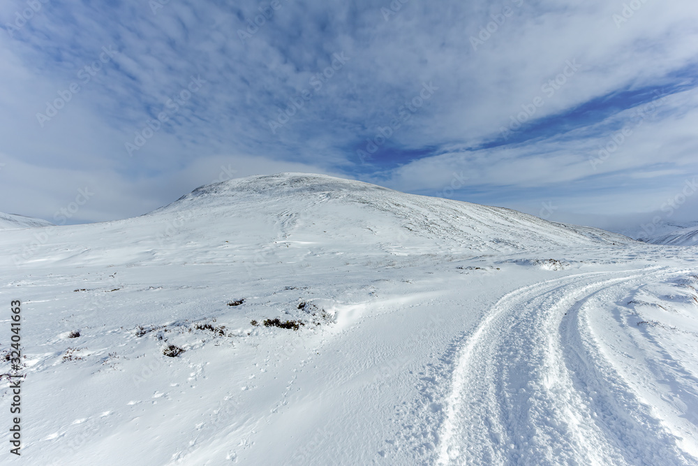 An scenic view of a moutain range in the winter with snowy slope under a majestic blue sky and some white clouds