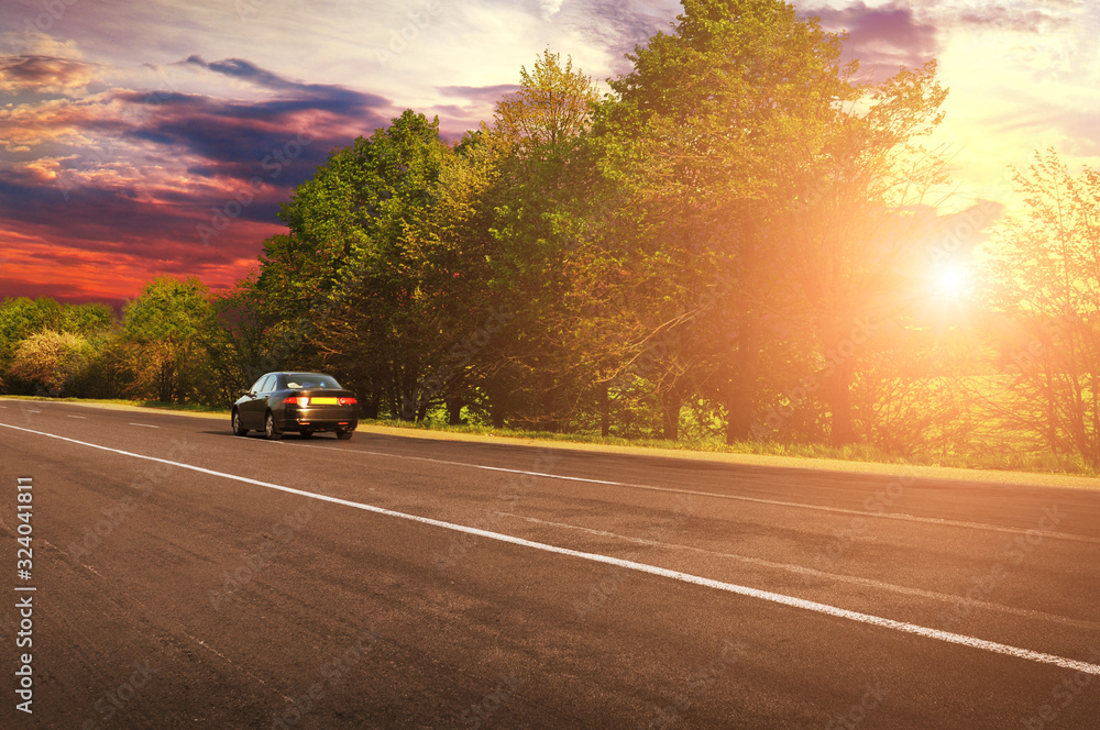 A black car on the countryside road against sky with sunset A black car on the countryside road against sky with sunset