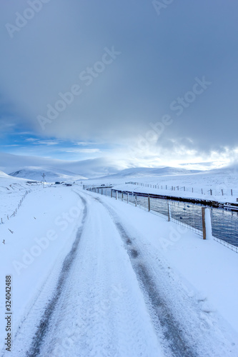 An scenic view of a moutain range in the winter with snowy slope and aqueduct under a majestic blue sky and some white clouds