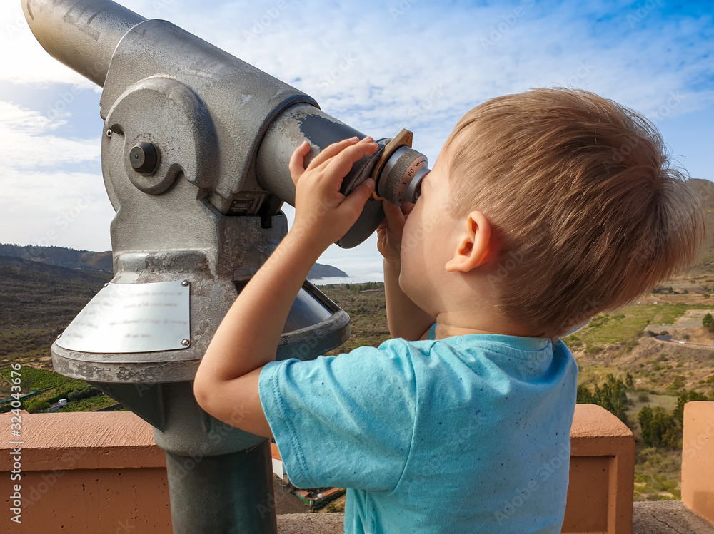 Portrait of little toddler boy looking in coin operated binoculars at beautiful mountain