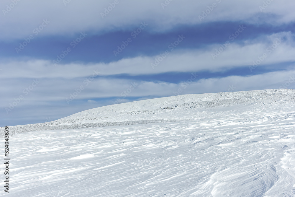 An scenic view of a moutain range in the winter with snowy slope under a majestic blue sky and some white clouds