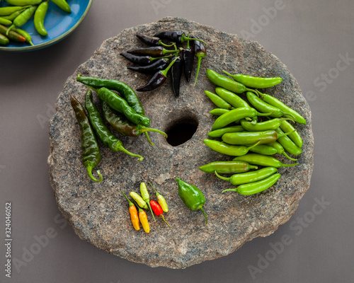 Variety of different chilies: serrano, habanero, tabasco, de cayene long slim, de cayene purple on stone with hole. Peppers in different stage of ripeness and pungency scale. photo