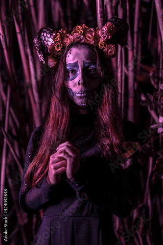 Halloween, a young girl dressed as a Mexican skull among bamboos, with purple lighting