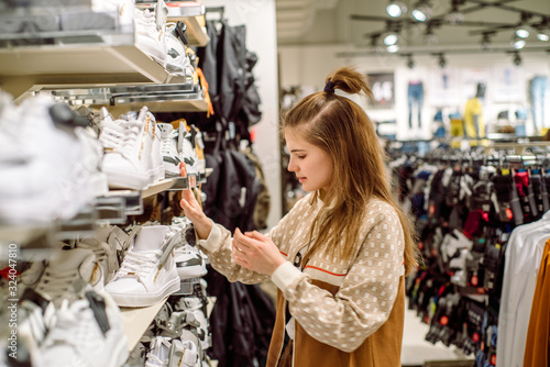 The teenager chooses white sneakers, beautiful shoes in the store.young woman buying it in Moll, casual shopping concept.