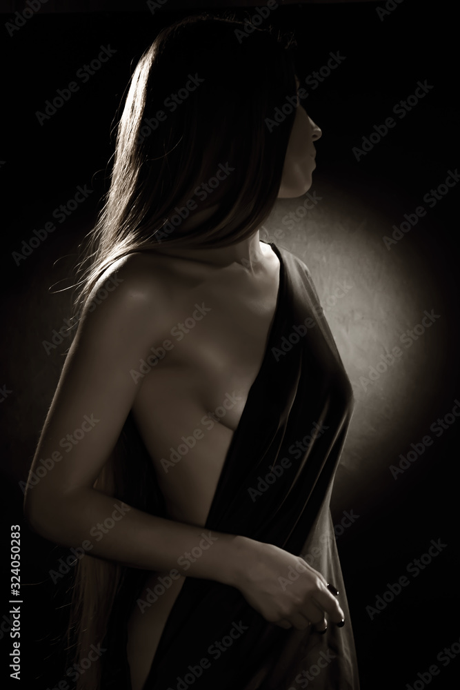 Artistic portrait of a young woman 25-30 years old with a deep neckline on the side on a dark background. Beauty and slimness of the female figure.