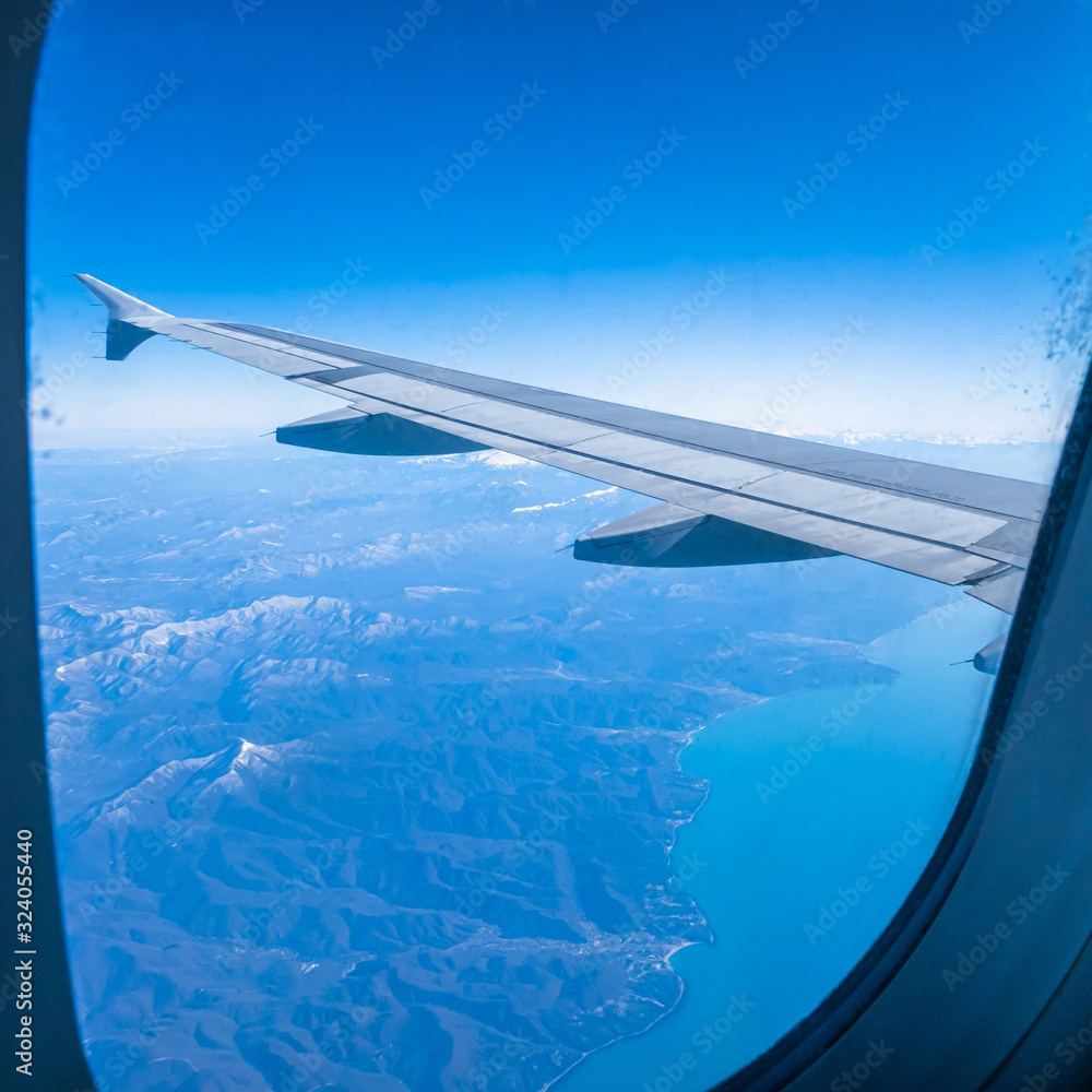 The wing of an airplane flying over the mountains and the sea