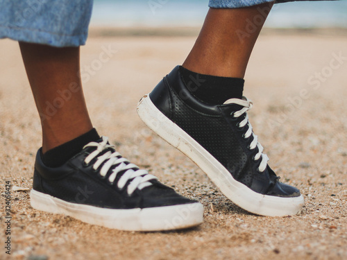Modelo posando zapatillas negras con bordes blancos, cordones blancos, medias negras, sobre arena de playa