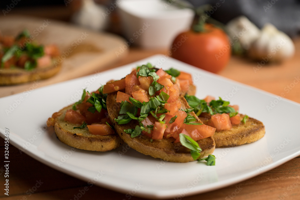 Italian bread with garlic, bruschetta with ham, basil and tomato served on a plate, close up shot Italian bread with garlic, bruschetta with ham, basil and tomato served on a plate, close up shot