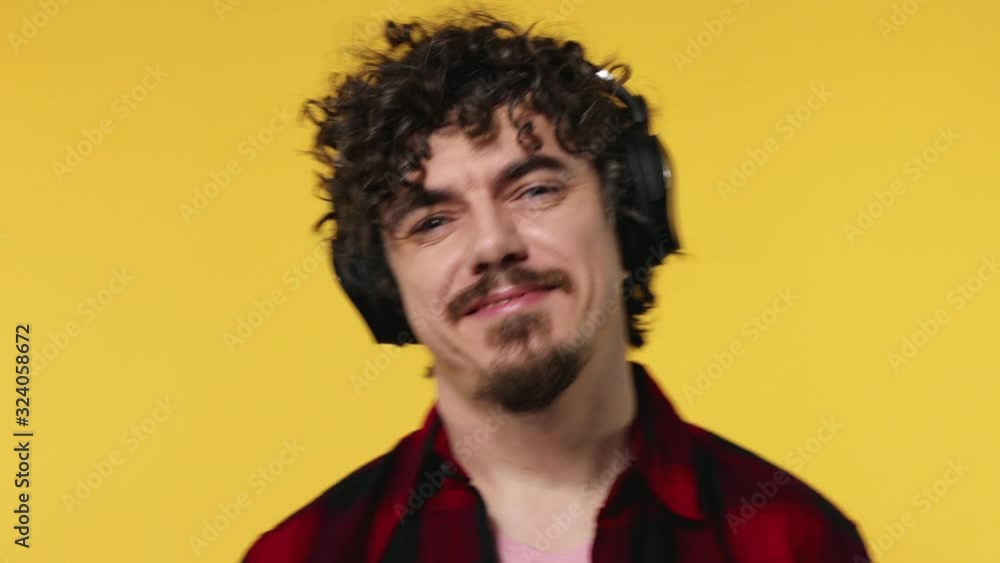 Handsome happy european man with beard in red shirt smiling and dancing isolated on yellow background. Guy in headphones listening to music. Lifestyle concept. Handsome happy european man with beard in red shirt smiling and dancing isolated on yellow background. Guy in headphones listening to music. Lifestyle concept.