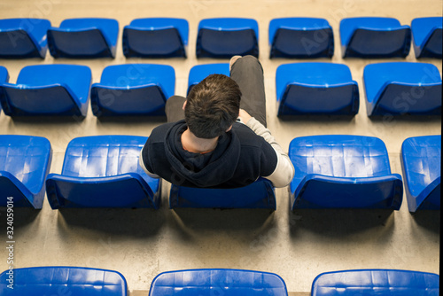 Caucasian boy, sitting in the stands of a pavilion at a sporting event.
