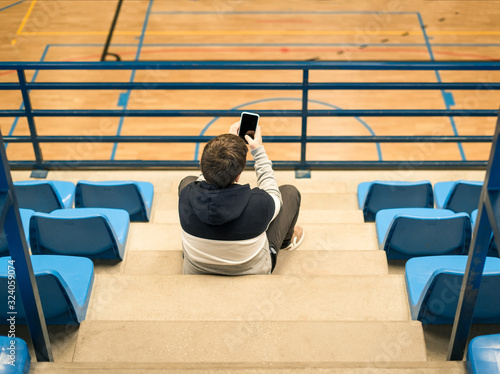 Caucasian boy, sitting in the stands of a pavilion at a sporting event. Recording with your mobile phone photo