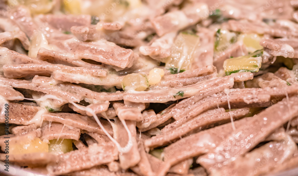 Very close up of the succulent and typical Italian dish Pizzoccheri in a white plate on a table. Typical dish from Valtellina, Lombardy, Italy.