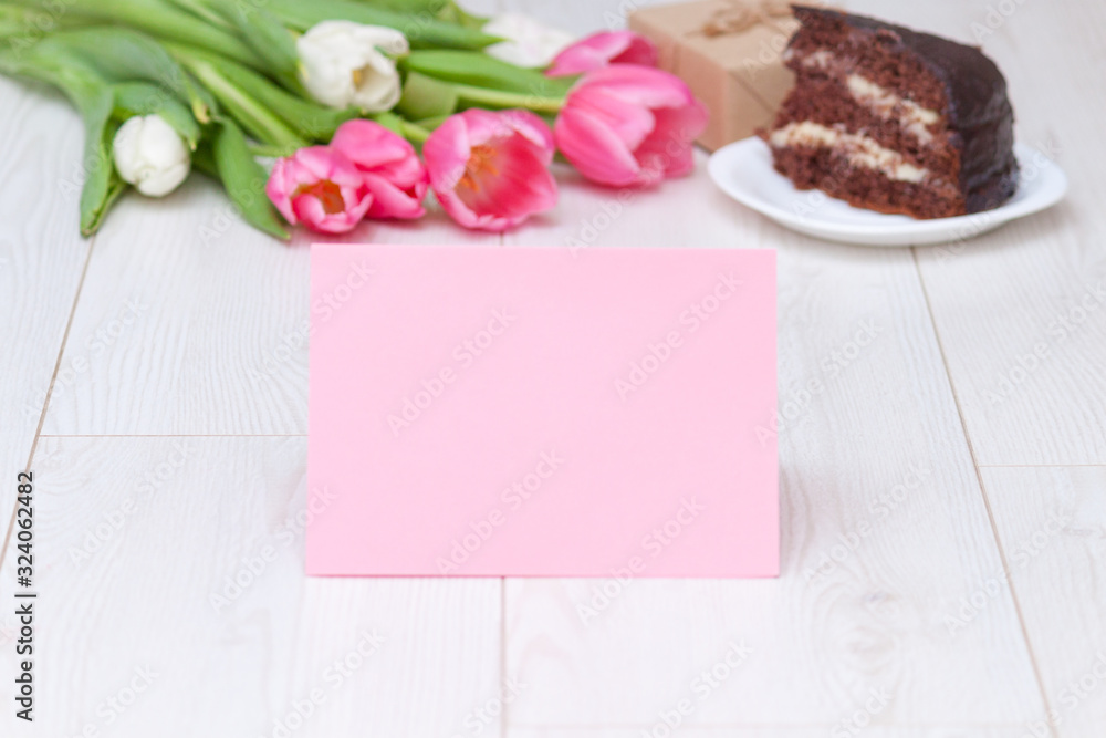 Paper card, bouquet of pink tulips, chocolate cake. pressent box on white wooden background. Copy space, close up. Mother's, women's day concept. Paper card, bouquet of pink tulips, chocolate cake. pressent box on white wooden background. Copy space, close up. Mother's, women's day concept.