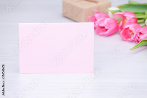 Spring pink tulips, gift box and empty paper card on white wooden background. Mother's, Women's Day concept.