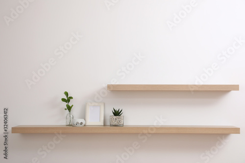 Wooden shelves with plants and photo frame on light wall