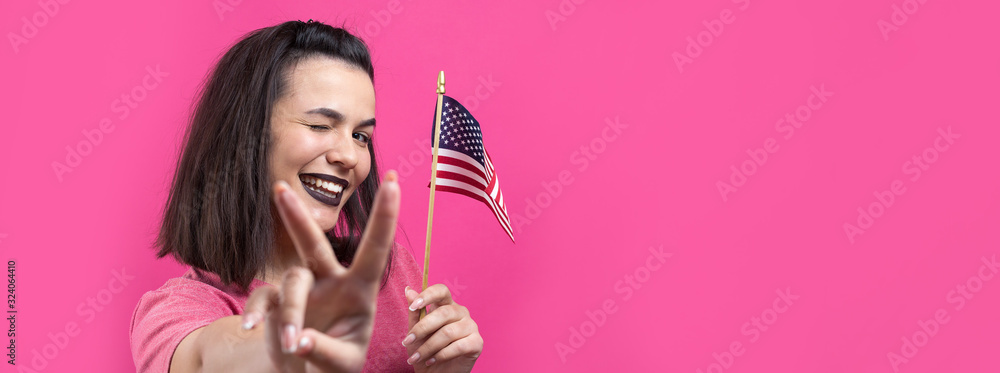 Happy young woman holding American flag against a studio pink background