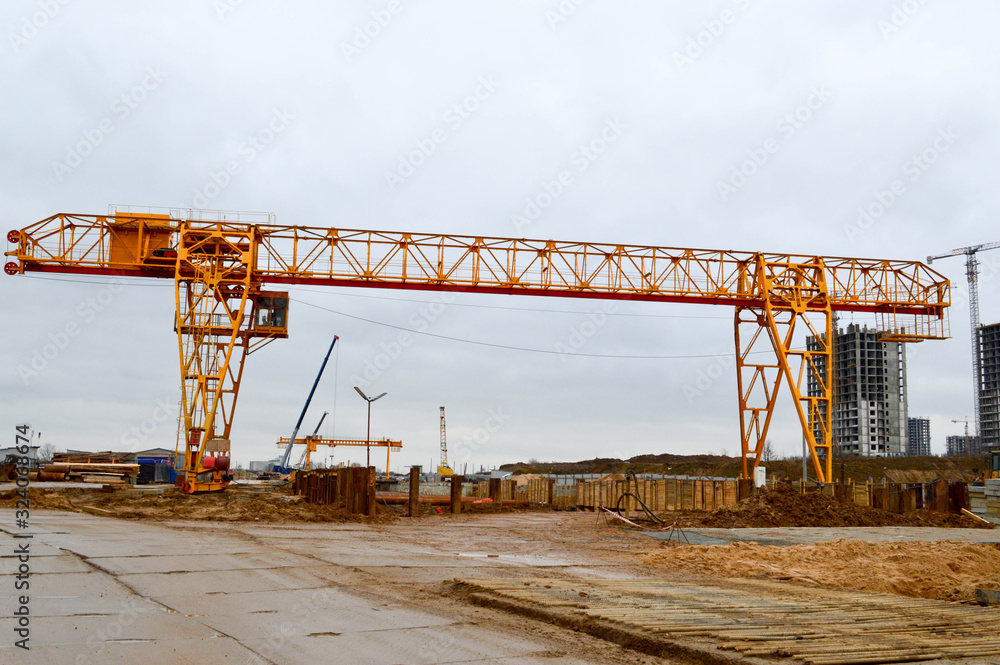 High heavy yellow metal iron load-bearing construction stationary industrial powerful gantry crane of bridge type on supports for lifting cargo on a modern construction site of buildings and houses