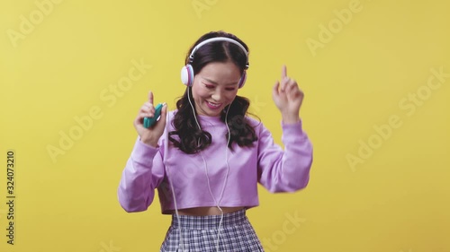 Excited pretty Asian hapanese fashion girl wearing wireless headphones and listening to enjoyable favorite music songs posing on yellow background. Studio shot. photo