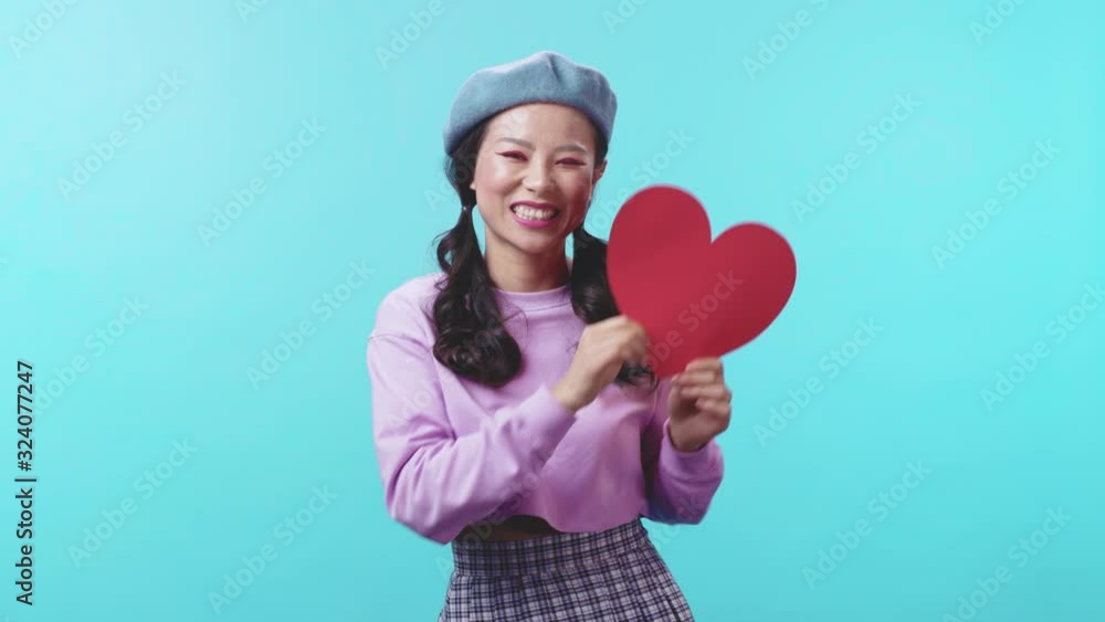 Romantic young Asian trendy girl holding a red paper heart smiling cheerful and flirting at camera on Valentine's Day. Feelings and emotions. Symbol of love. Romantic young Asian trendy girl holding a red paper heart smiling cheerful and flirting at camera on Valentine's Day. Feelings and emotions. Symbol of love.